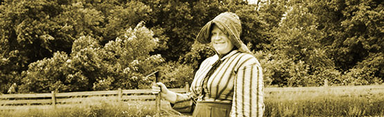 A woman stands in a field wearing traditional dress and bonnet.