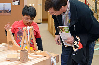 A child experiments with a ball and a ramp, while an adult watches.