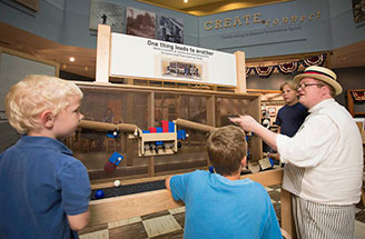 A man in period costume explains a ball chute exhibit.